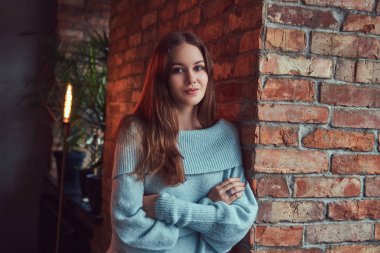 Çatı katı iç ile bir odada bir tuğla duvara yaslanmış bir gri süveterli şehvetli bir esmer.