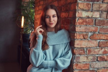 Çatı katı iç ile bir odada bir tuğla duvara yaslanmış bir gri süveterli şehvetli bir esmer.