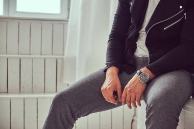 Rahat yakışıklı genç bir adam şık giysiler ve bir şömine üzerinde oturan kol saati.