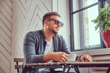 İçme kahve kahve dükkanında yakışıklı bir genç adam güneş gözlüğü ve rahat giysiler.