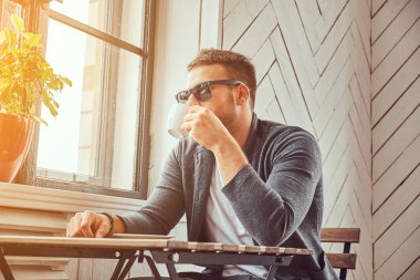 İçme kahve kahve dükkanında yakışıklı bir genç adam güneş gözlüğü ve rahat giysiler.