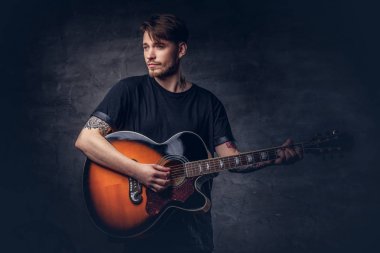 Akustik gitar, karanlık bir arka plan üzerinde izole çalmaya siyah t-shirt bir çekici dövmeli gitarist.