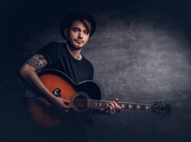 Çekici bir gitarist akustik gitar, karanlık bir arka plan üzerinde izole çalmaya şapkalı dövme.