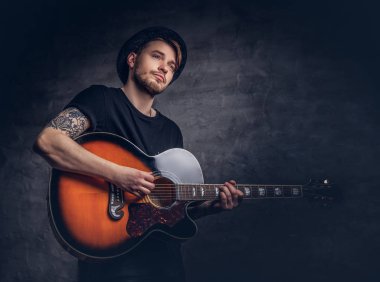 Çekici bir gitarist akustik gitar, karanlık bir arka plan üzerinde izole çalmaya şapkalı dövme.