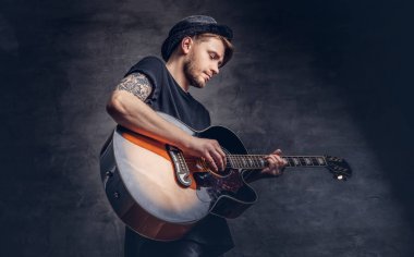 Çekici bir gitarist akustik gitar, karanlık bir arka plan üzerinde izole çalmaya şapkalı dövme.