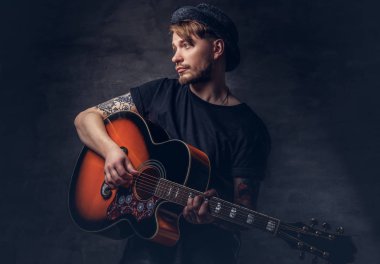 Çekici bir gitarist akustik gitar, karanlık bir arka plan üzerinde izole çalmaya şapkalı dövme.