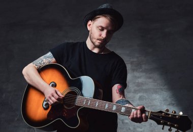 Çekici bir gitarist akustik gitar, karanlık bir arka plan üzerinde izole çalmaya şapkalı dövme.