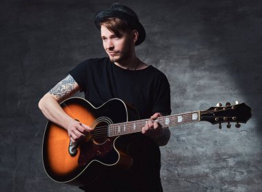 Çekici bir gitarist akustik gitar, karanlık bir arka plan üzerinde izole çalmaya şapkalı dövme.