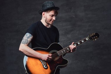 Çekici bir gitarist akustik gitar, karanlık bir arka plan üzerinde izole çalmaya şapkalı dövme.