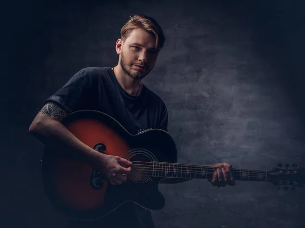 一个迷人的纹身吉他弹奏者在黑色 T恤上演奏的声学吉他 孤立在黑暗的背景下 — 图库照片