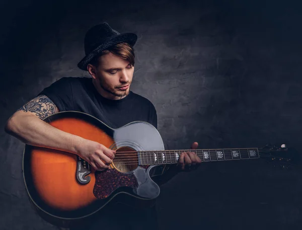 一个迷人的纹身吉他弹奏者在吉他上演奏 在黑暗背景下孤立 — 图库照片