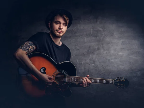 Atraente Guitarrista Tatuado Chapéu Tocando Guitarra Acústica Isolado Fundo Escuro — Fotografia de Stock