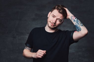 Karanlık bir arka plan üzerinde siyah bir t-shirt giymiş dövmeli kollu yakışıklı bir moda erkek portresi Studio izole.