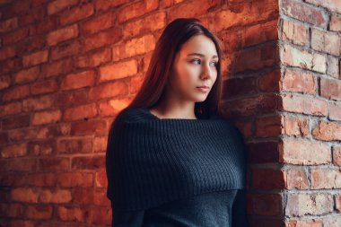 Yakın çekim portre Siyah kazaklı çatı iç ile bir odada bir tuğla duvara yaslanmış güzel bir sevimli esmer.