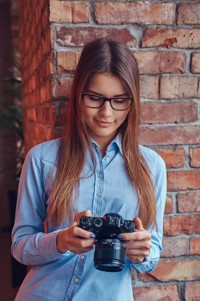 ロフト デザインの客室で レンガの壁の眼鏡と青のシャツにもたれて若い女性写真家の肖像画 — ストック写真