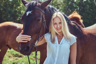 Beyaz bir bluz ve yeşil bir alana bir at sarılma kot giyen sevimli güzel sarışın.