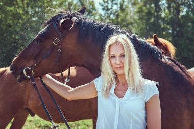 Beyaz bir bluz ve yeşil bir alana bir at sarılma kot giyen sevimli güzel sarışın.