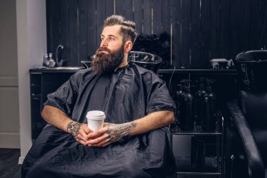 Saç yıkama önce bir kuaför salonu yakışıklı sakallı adam kollarını bir dövme ile kahve içer.