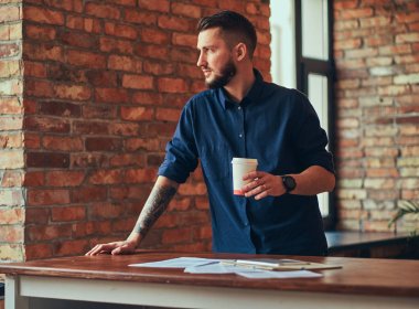 Mavi gömlek ayakta çatı iç ile bir odada sakallı bir işadamı portresi.