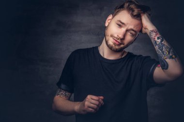 Karanlık bir arka plan üzerinde siyah bir t-shirt giymiş dövmeli kollu yakışıklı bir moda erkek portresi Studio izole.