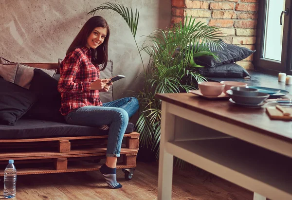 Charming brunette in a flannel shirt and jeans sitting on a couch