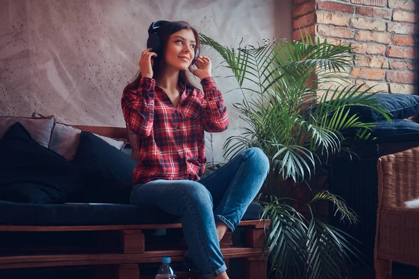 Portrait of a sexy brunette in a flannel shirt and jeans listening to music