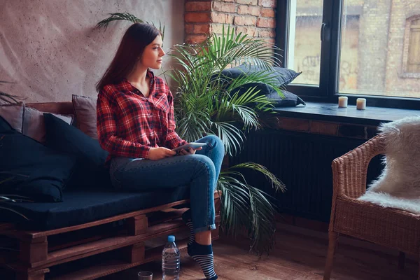 Charming brunette in a flannel shirt and jeans sitting on a couch