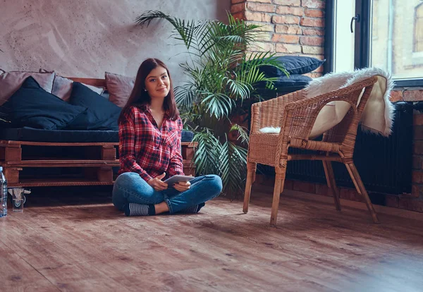 Charming brunette in a flannel shirt and jeans sitting on a floor