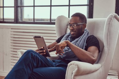 Genç bir öğrenci bir sandalye ve bir tablet kullanarak oturur.