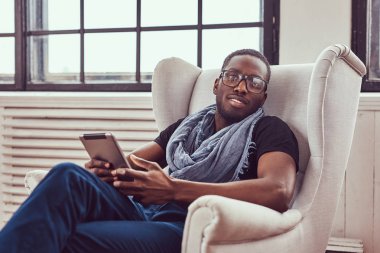 Genç bir öğrenci bir sandalye ve bir tablet kullanarak oturur.