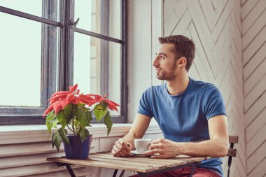 Genç bir öğrenci bir pencerede otururken sabah kahve içer.