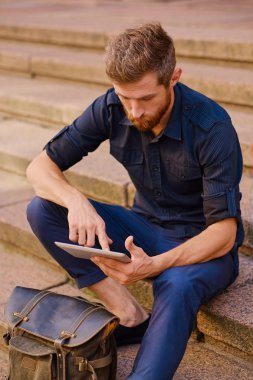 Tablet bilgisayar ile rahat kıyafetler içinde yakışıklı sakallı erkek