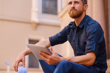 Tablet bilgisayar ile rahat kıyafetler içinde yakışıklı sakallı erkek