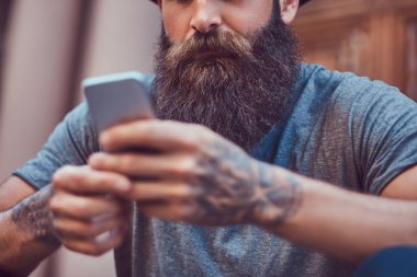 Yakışıklı hippi erkek şık sakal ve kollarını rahat kıyafetler giymiş ve merdiven üstünde otururken smartphone kullanarak bir dövme ile.