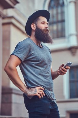 Yakışıklı hippi erkek bir şık sakal ve kollarını rahat kıyafetler giymiş ve telefon kullanarak dövme.