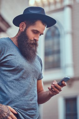 Yakışıklı hippi erkek bir şık sakal ve rahat kıyafetler giymiş ve telefon kullanarak kolundaki dövme.