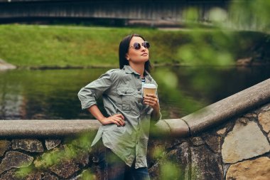 Esmer hippi kız rahatlatıcı bir fincan kahve bir nehir şehrin karşı ile.