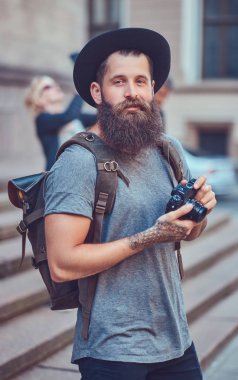 Bir fotoğraf makinesi kullanarak rahat kıyafetler içinde yakışıklı hippi erkek bir şık sakal ve kollarını dövme ile giyinmiş.