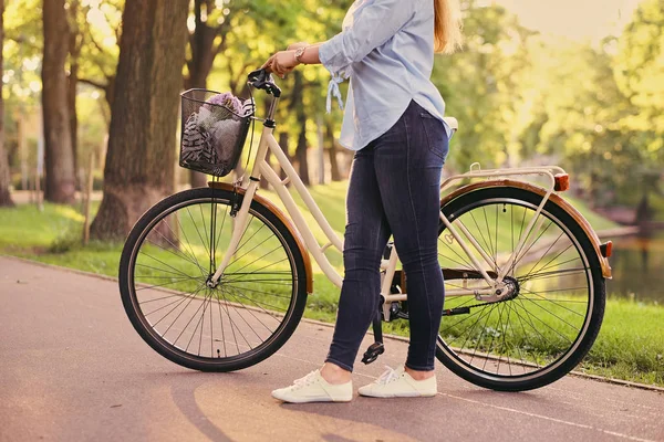 Een aantrekkelijke brunette vrouw met een fiets in het stadspark. — Stockfoto