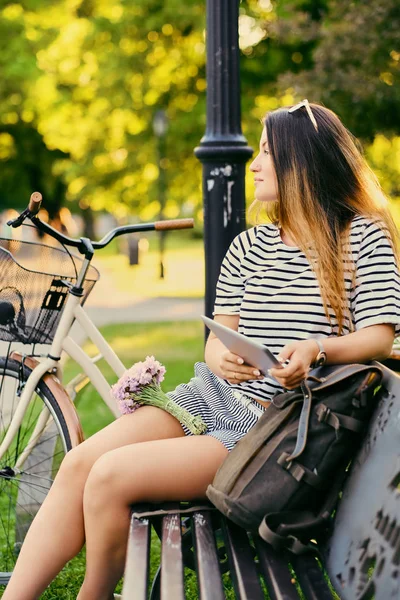 Retrato de uma morena atraente se senta em um banco com bicicleta — Fotografia de Stock