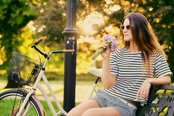 Portret van een aantrekkelijke brunette zit op een bankje met fiets — Stockfoto