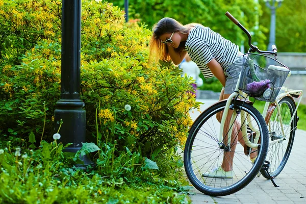En attraktiv brunett kvinna med en cykel som sniffar blommor i — Stockfoto