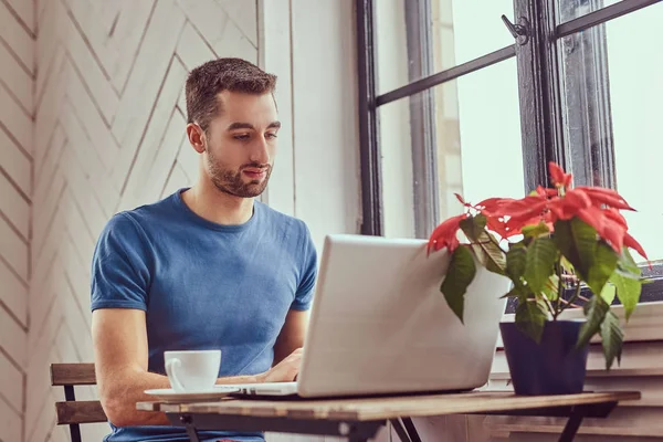 Un joven estudiante caucásico bebe café de la mañana trabajando con una l —  Fotos de Stock