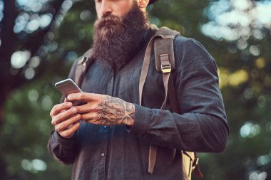 Telefonu kullanma yakışıklı hipster seyahat bir şık sakal ve kollarını rahat kıyafetler ve şapka giymiş dövme.