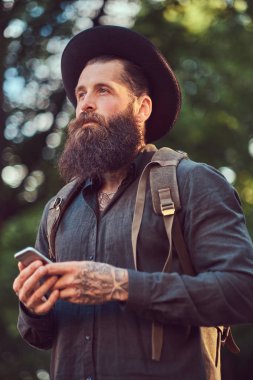 Telefonu kullanma yakışıklı hipster seyahat bir şık sakal ve kollarını rahat kıyafetler ve şapka giymiş dövme.
