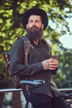 Telefonu kullanma yakışıklı hipster seyahat bir şık sakal ve kollarını rahat kıyafetler ve şapka giymiş dövme.