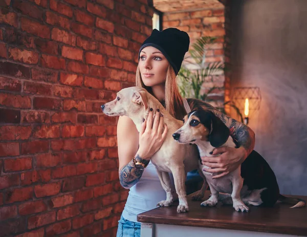 A stylish tattooed blonde female in t-shirt and jeans with her dogs