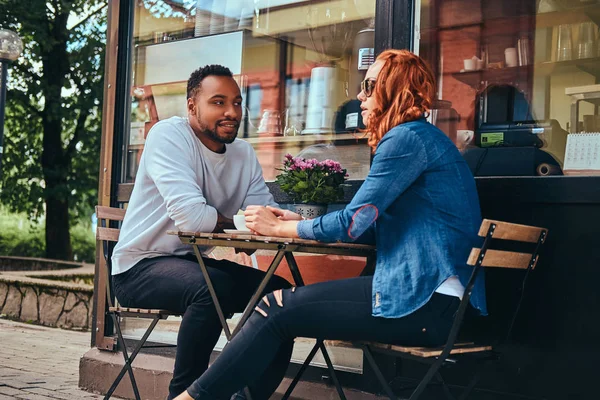 Couple dating drinking coffee, sitting near the coffee shop. Outdoors on a date.