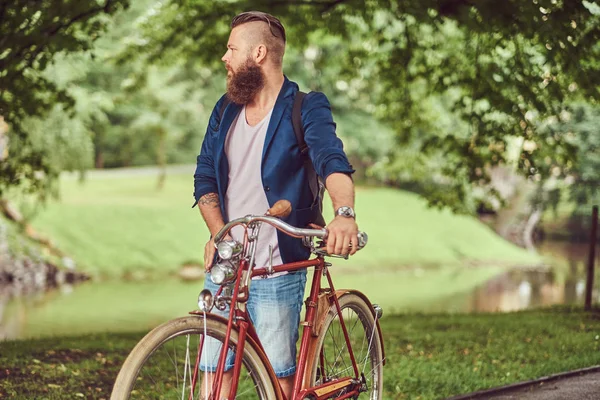Viajero vestido con ropa casual con una mochila, relajarse en un parque de la ciudad después de montar en una bicicleta retro . — Foto de Stock