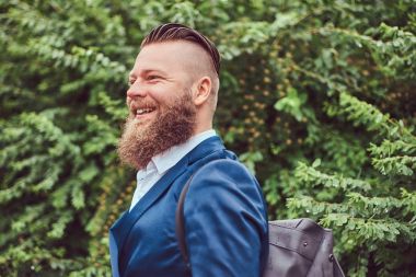 Bir gömlek ve ceket bir parkta duran bir sırt çantası ile giyinmiş bir saç kesimi ile sakallı bir erkek portresi.